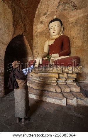 BAGAN, MYANMAR - 14 JAN, 2014: Unidentified Burmese man brings religious offerings to Buddha statue inside one of pagoda ruins at Bagan Kingdom, Myanmar (Burma)