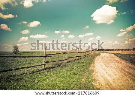 Sunny day in countryside. Empty rural road going through summer landscape under blue cloudy sky. Nature background in vintage style