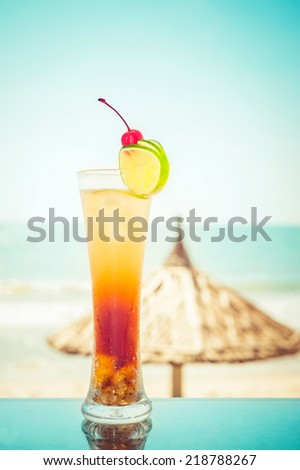 Long Island cocktail with fruits decoration at tropical ocean beach with umbrella. Vintage style, hipster colors image with copy space for party invitation text