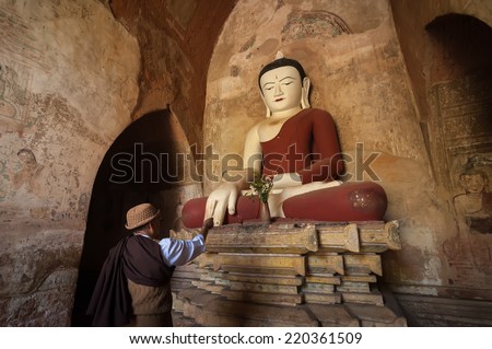 BAGAN, MYANMAR - 14 JAN, 2014: Unidentified Burmese man brings religious offerings to Buddha statue inside one of pagoda ruins at Bagan Kingdom, Myanmar (Burma)