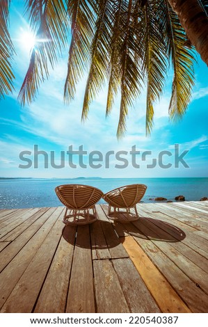 Amazing tropical beach landscape with palm tree and chairs for relaxation on wooden terrace. Travel background in vintage style