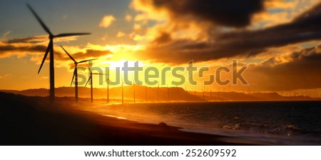 Wind turbine power generators silhouettes at ocean coastline at sunset. Alternative renewable energy production in Philippines. Two images panorama, tilt shift effect