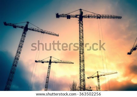 Abstract Industrial background with construction cranes silhouettes over amazing sunset sky