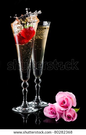 Two glasses of sparkling splashing wine (champagne) with pink roses and strawberry on black