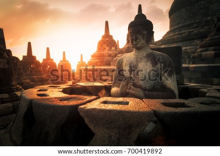 Amazing sunrise view of meditating Buddha statue and stone stupas against shining sun on background. Ancient Borobudur Buddhist temple. Great religious architecture. Magelang, Central Java, Indonesia