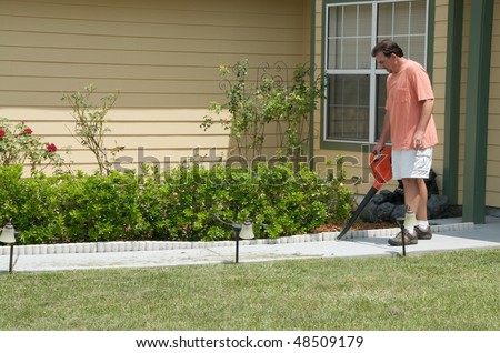 Caucasian male blowing lawn clippings from the sidewalk in front of a single family residence. Close up.