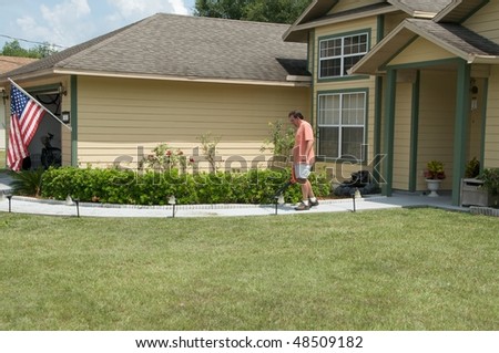 Caucasian male blowing lawn clippings from the sidewalk in front of a single family residence.