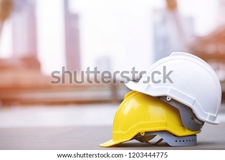 yellow and white hard safety wear helmet hat in the project at construction site building on concrete floor on city with sunlight. helmet for workman as engineer or worker. concept safety first.
