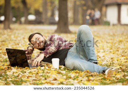 Urban Man Laying Down In Autumn Falling Leaves Using Laptop Computer Outdoor