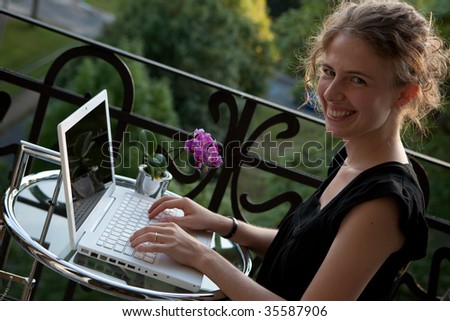 portrait of a smiling young woman writing on a white modern laptop computer on a balcony in art nouveau