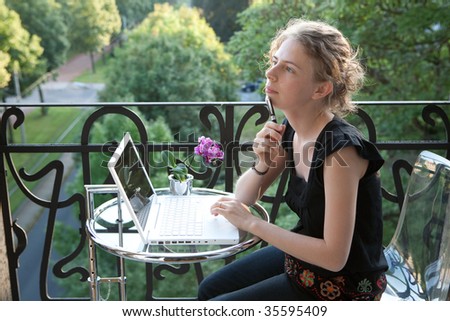 young woman writing on a white modern laptop computer on a balcony in art nouveau
