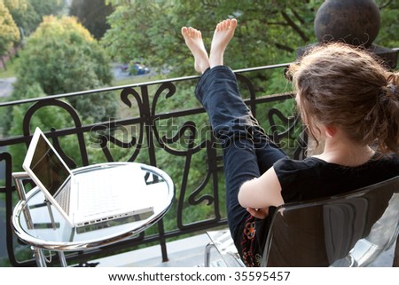 young woman relaxing with a white modern laptop computer on a balcony in art nouveau