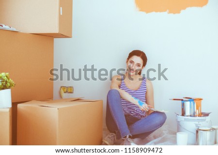 Woman choosing paint colour from swatch for new home sitting on wooden floor. Woman in the house