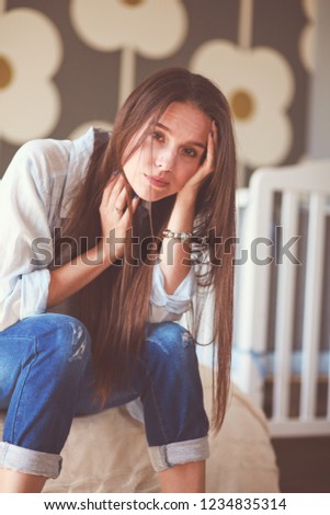 Young tired woman sitting on the bed near children\'s cot. Young mom.