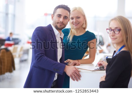 Sales situation in a car dealership, the young couple is signing the sales contract to get the new car