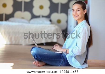 Young woman sitting on the floor near children\'s cot with laptop. Young mom