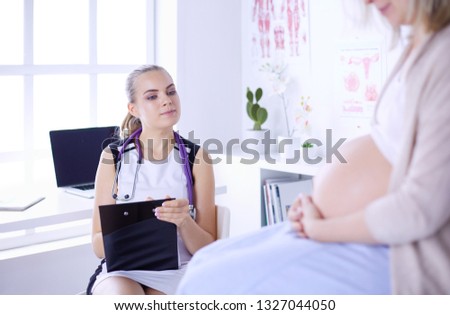 Young woman doctor with stethoscope and tablet speaking with pregnant woman at hospital.