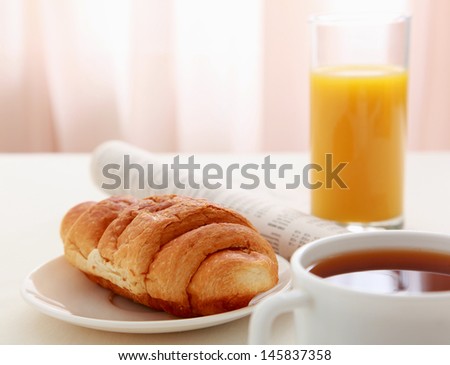 Glass of refreshing orange fruit juice and croissant over business paper