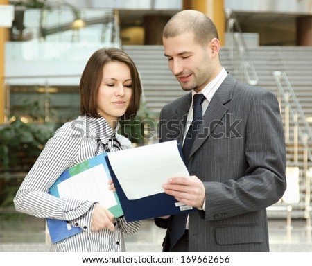 Portrait of two business people standing in the office looking into folder with business plan
