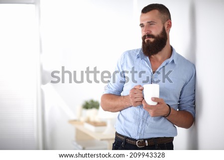 Young man  standing near wall and holding cup of coffee in office