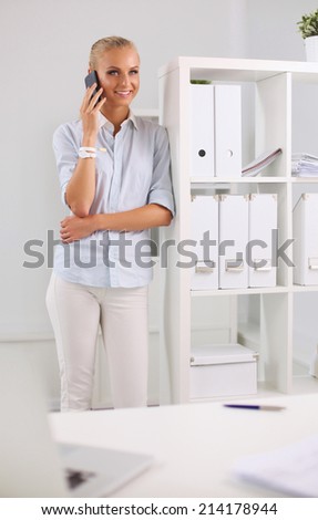 Young business woman standing in office talking on her mobile