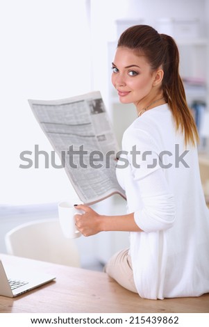 Cute businesswoman holding newspaper sitting at her desk in bright office