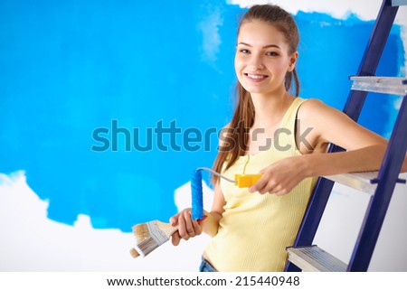 Happy beautiful young woman doing wall painting, sitting on ladder