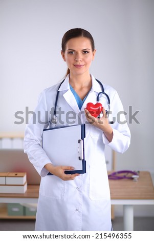Young woman doctor holding folder and  a red heart, isolated on white background