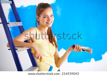 Happy beautiful young woman doing wall painting, sitting on lad