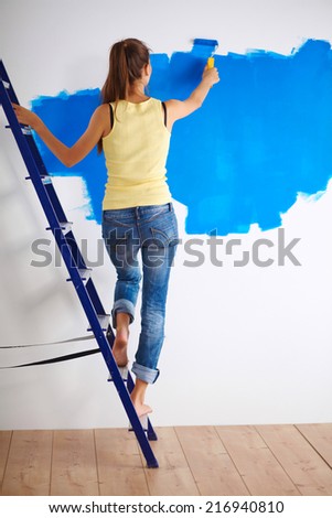 Happy beautiful young woman doing wall painting, standing on la