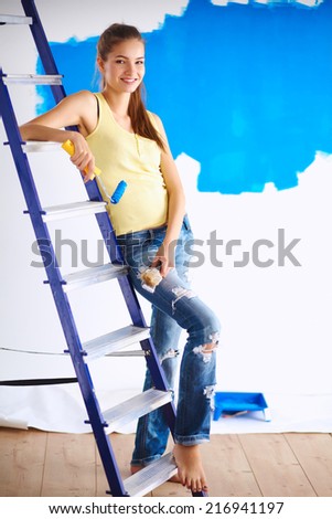 Happy beautiful young woman doing wall painting, standing near