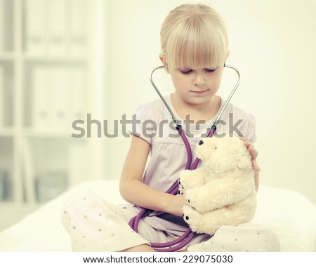 Little girl is examining her teddy bear using stethoscope, isolated