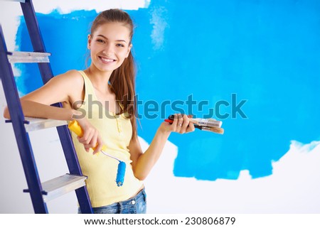 Beautiful young woman doing wall painting, sitting on ladder