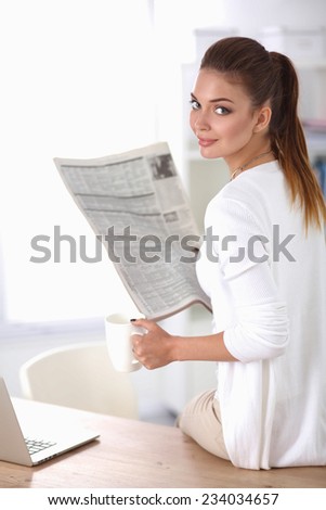 Cute businesswoman holding newspaper sitting at her desk in office