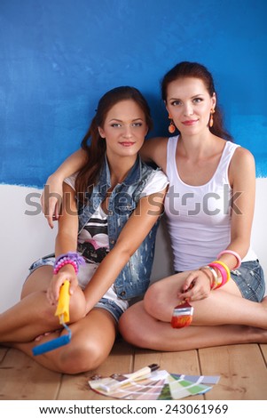 Two Beautiful young woman doing wall painting, sitting