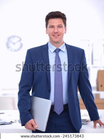 Business man or manager standing against his desk at the office isolated