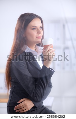 Woman drink coffee at office, standing near desk .