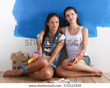Two beautiful young woman doing wall painting, sitting
