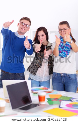 Young business people standing at office near desk and showing ok.