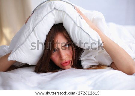 Female lying on bed and closing her ears with pillow.