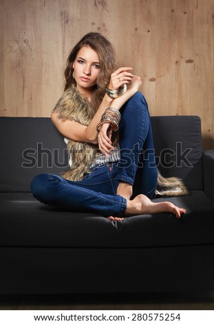 Portrait of a elegant woman sitting on a black sofa wearing a blue jeans and fur vest