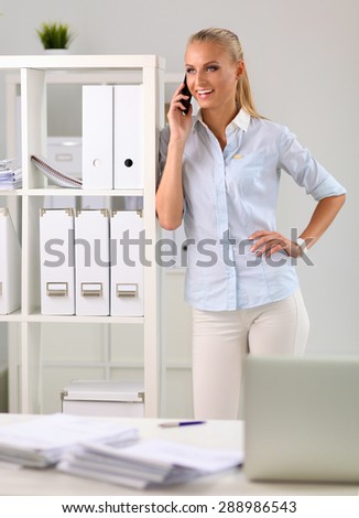 Young business woman standing in office talking on her mobile phone.