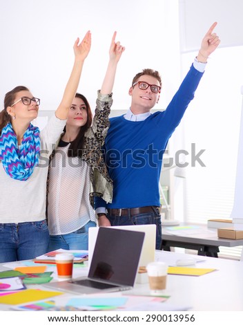 Young business people standing at office near desk and pointing up.