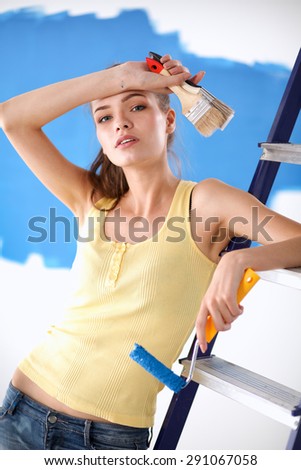 Beautiful young woman doing wall painting, standing near ladder.