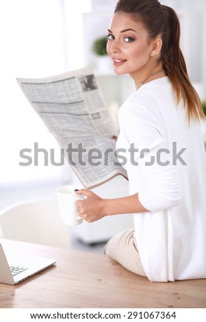 Cute businesswoman holding newspaper sitting at her desk in office .