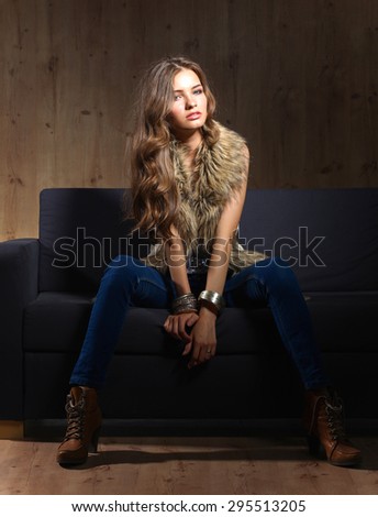 Portrait of a elegant woman sitting on a black sofa wearing a blue jeans and fur vest