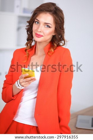 Beautiful businesswoman using cell phone standing in office, isolated