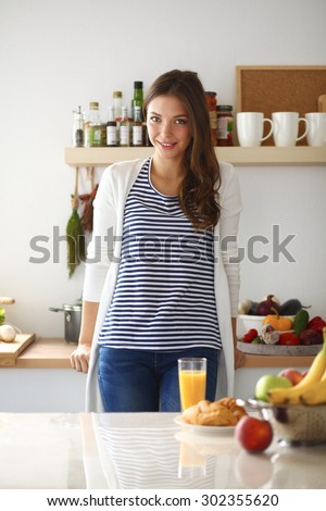 Young woman with glass of juice and cakes standing in kitchen .