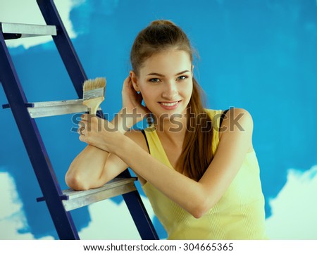 Beautiful young woman doing wall painting, standing near ladder