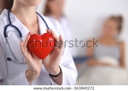 Young woman doctor holding a red heart, standing on gray background